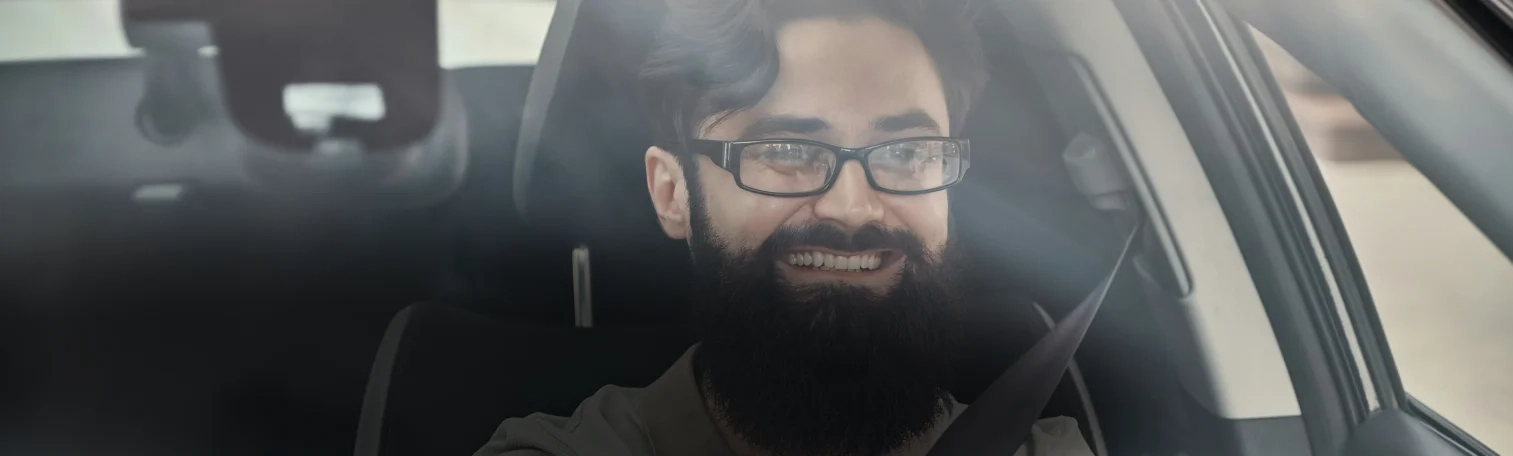 A man with eyeglasses smiling while driving a car.