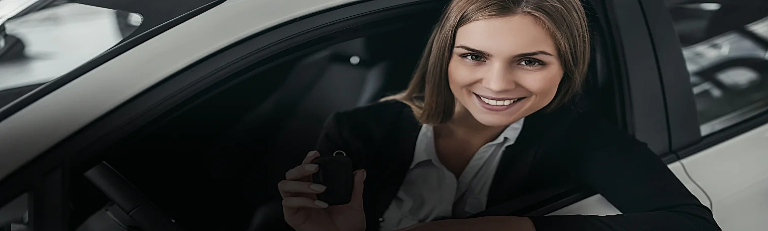 A blonde hair woman holding a car key while inside a white car.